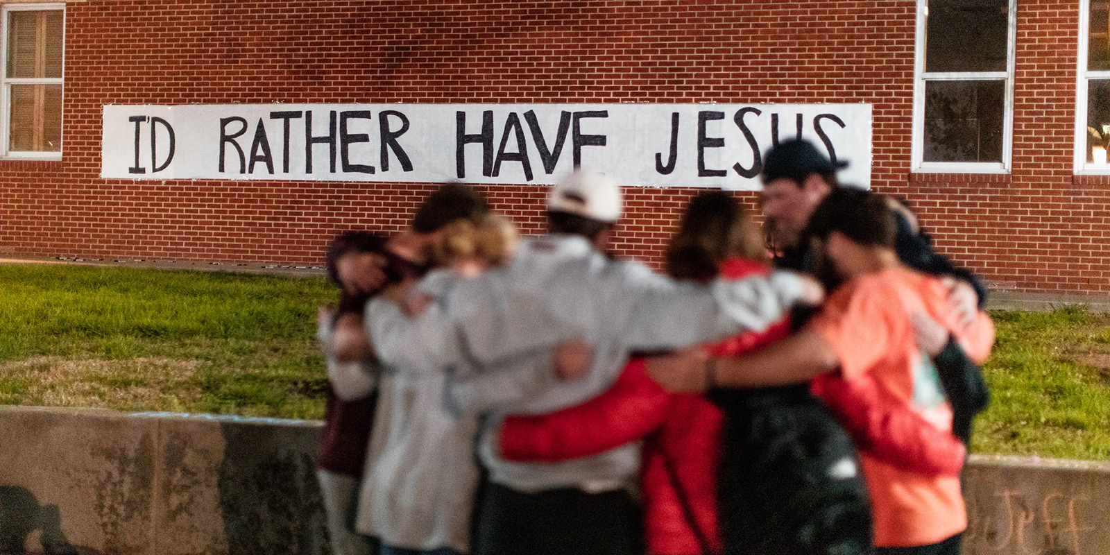 Students pray together on Fountain Mall in front of a sign that reads "I'd rather have Jesus"