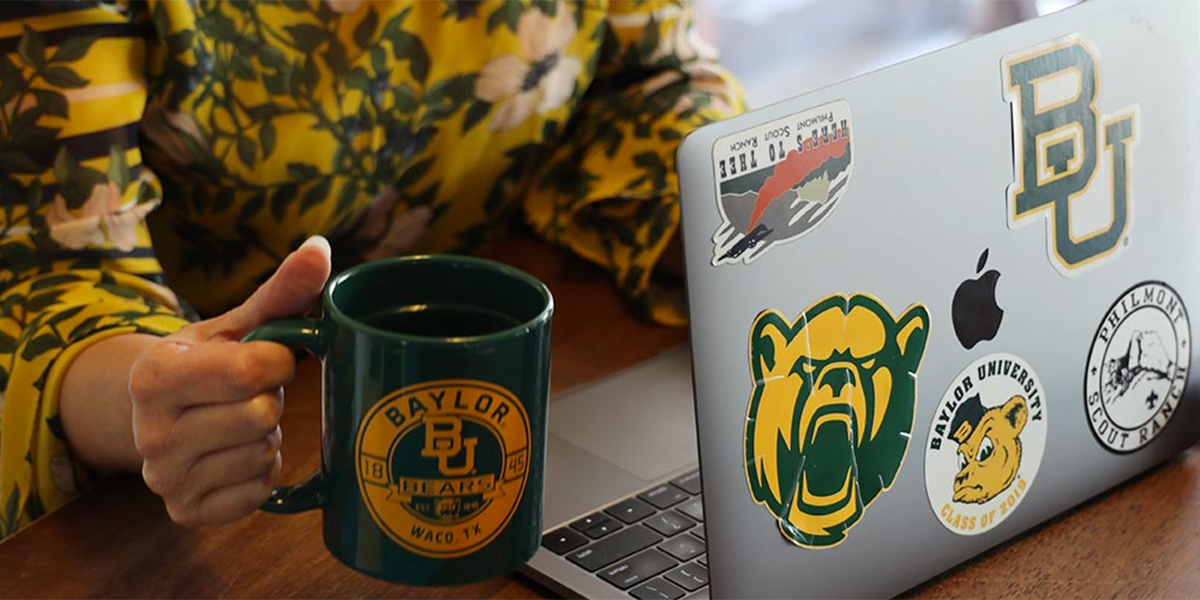 A person sitting to work on a laptop covered with Baylor stickers