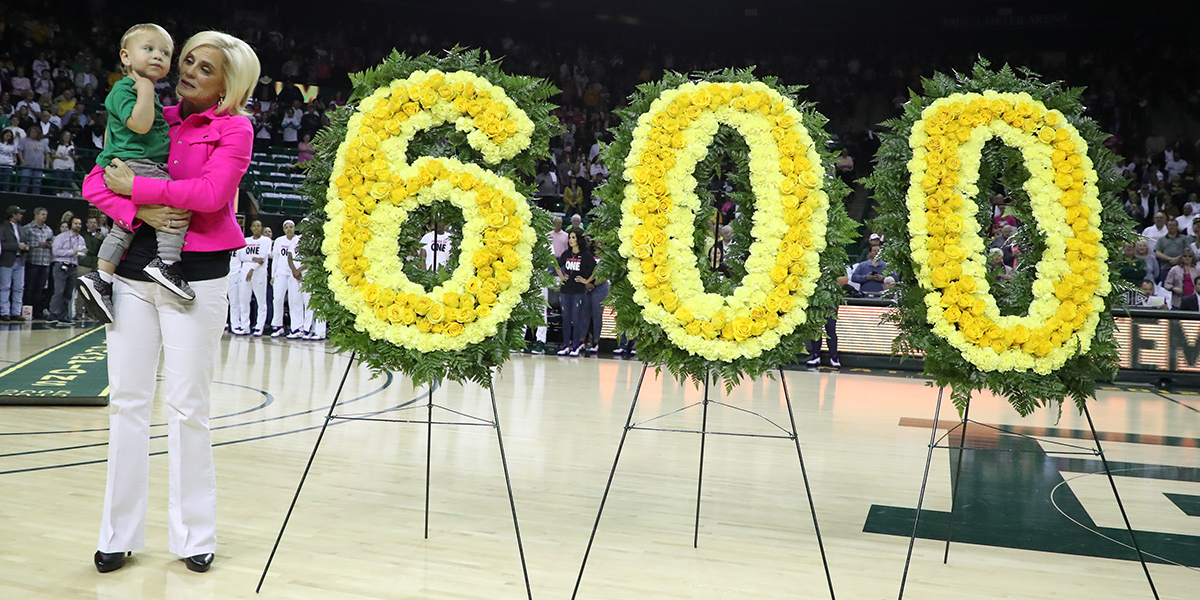 Kim Mulkey on the court with her grandson and flowers honoring her 600th career win