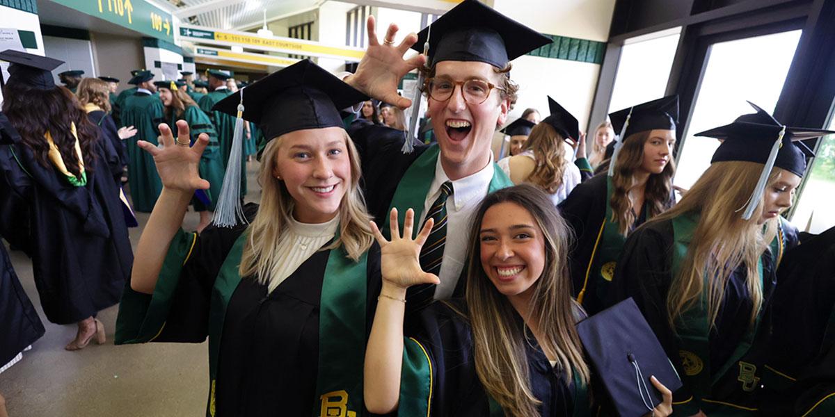 Three new Baylor graduates do a "sic 'em" in the Ferrell Center corridor